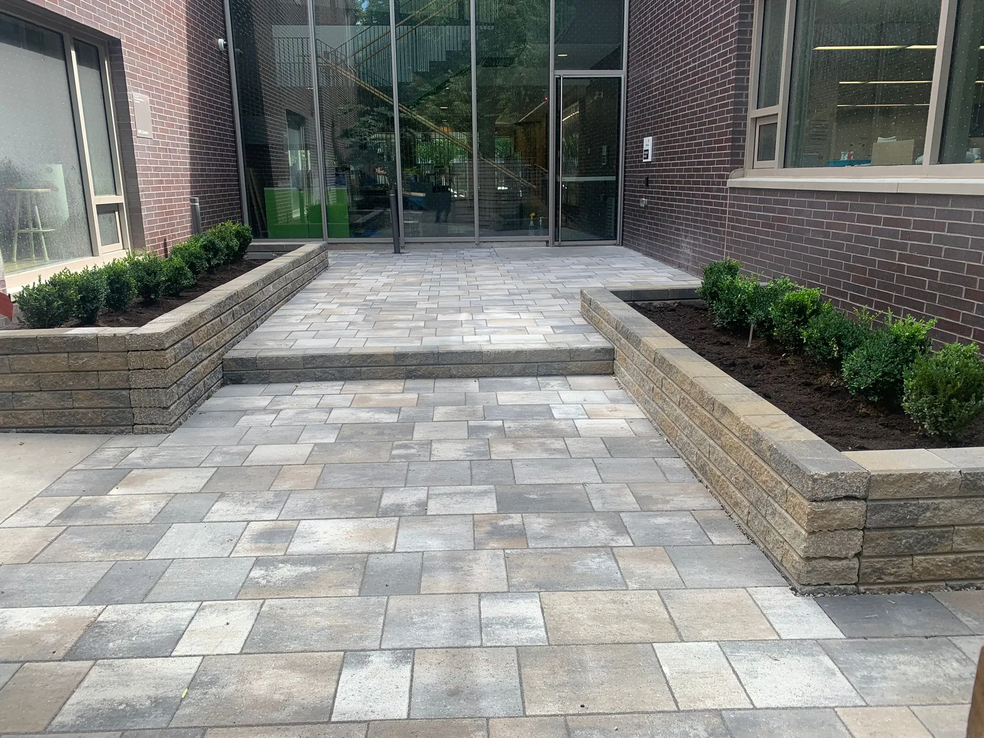Large-format paver plaza with raised planters at a modern building entrance