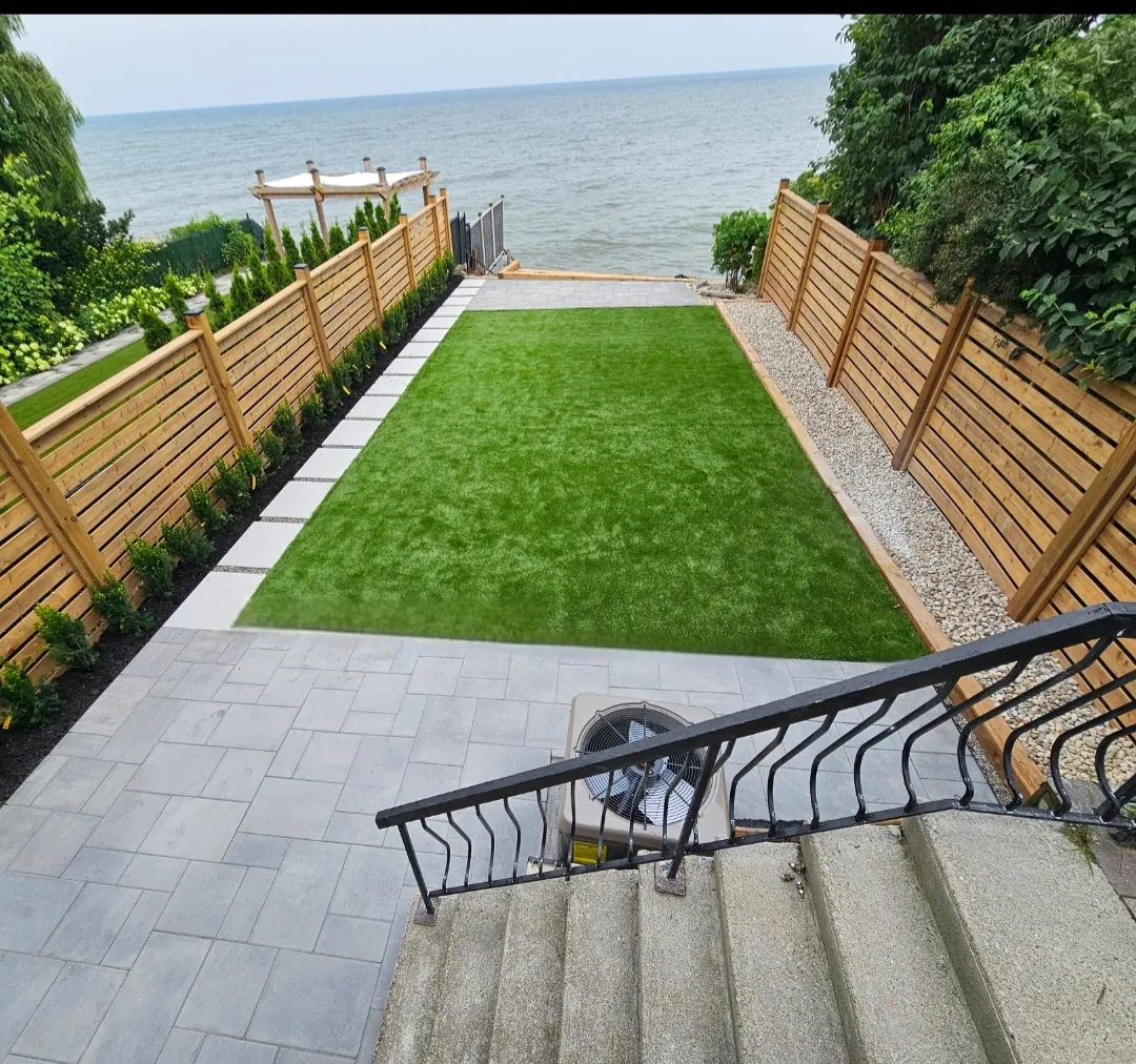 Stone stairs leading down to an artificial turf yard framed by cedar fencing beside the lake