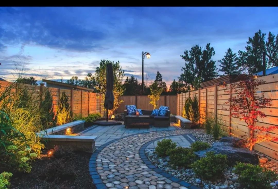 Backyard patio with paver pathway, seating and garden lighting at dusk